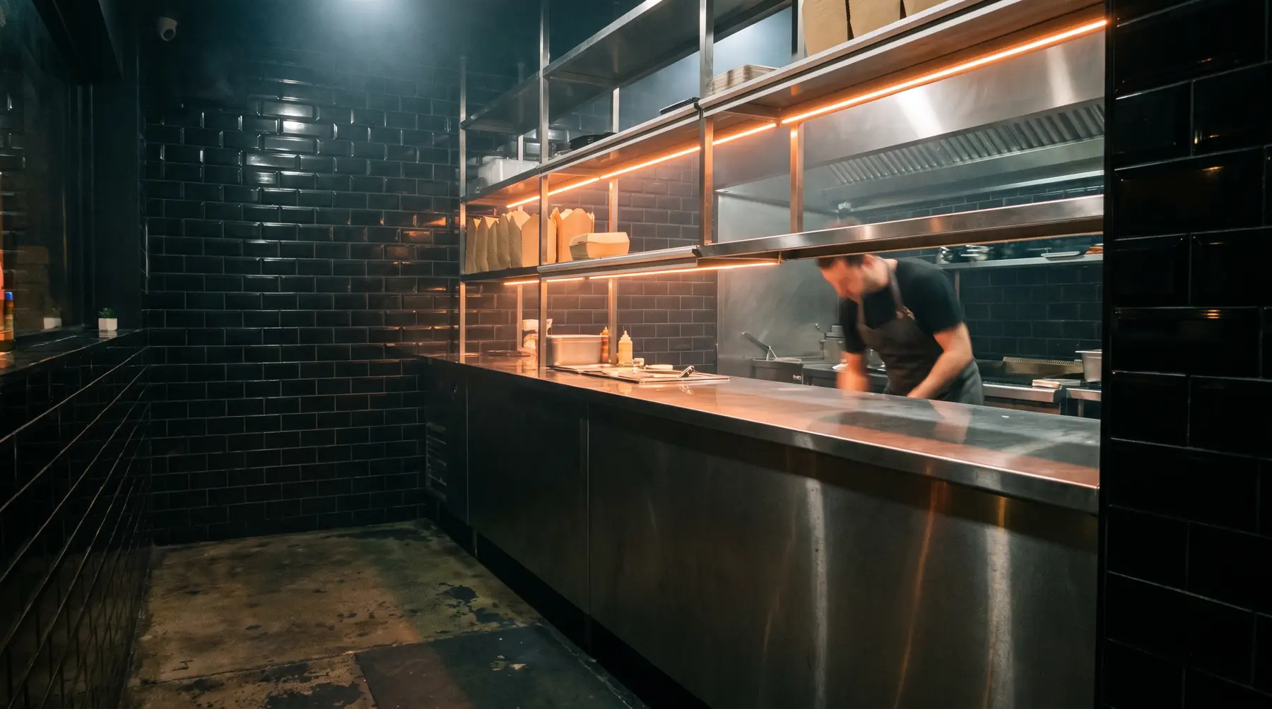 The counter at night — black tile, stainless pass, warm orange light